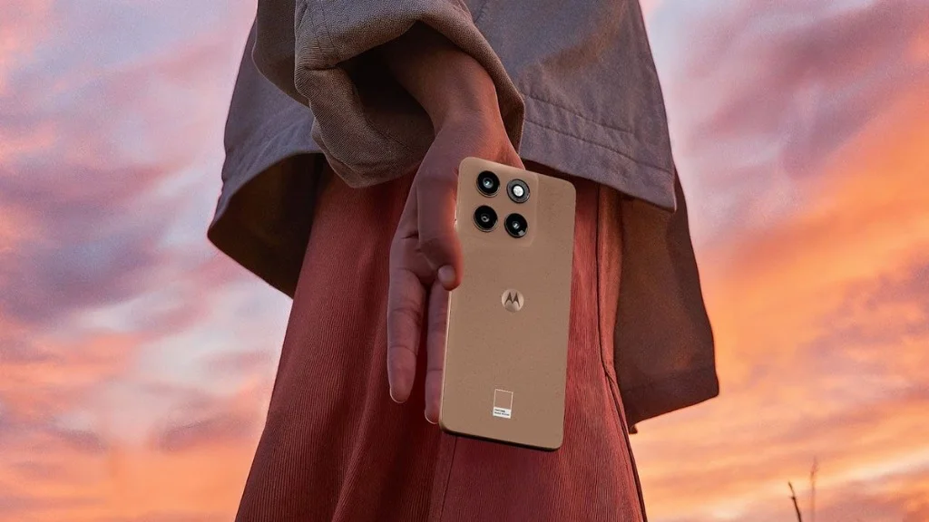 Pessoa segurando o Motorola Edge 70 Fusion na cor cobre/pêssego contra um céu no pôr do sol